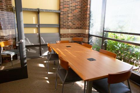 Non Profit meeting room with conference table, chairs, and brick wall and large window on the other wall