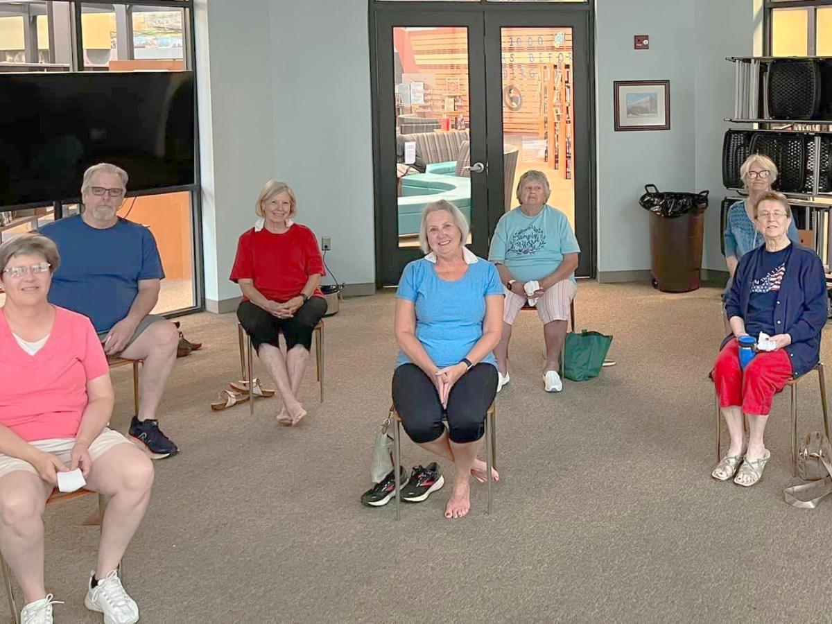 around a half dozen men and women sit in chairs in exercise clothes, they are smiling